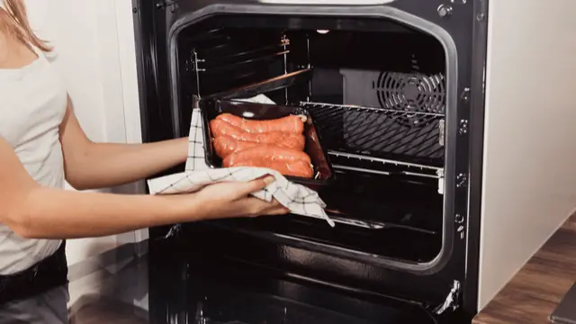 woman with a pan full of sausages putting them in an oven