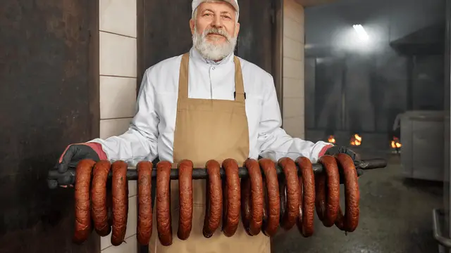 older employee standing in smokehouse with smoked sausages